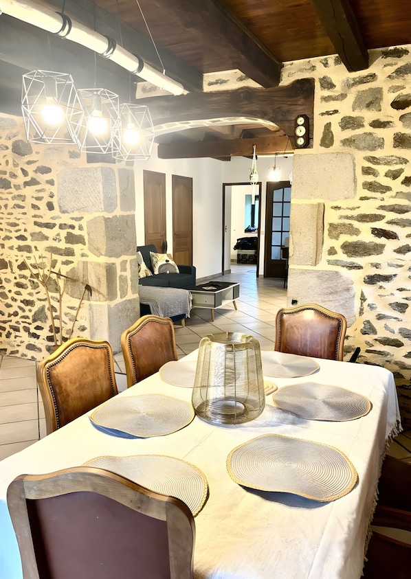 Un comedor con pared de piedra, vigas de madera en el techo y una mesa decorada con individuales y un florero de cristal.