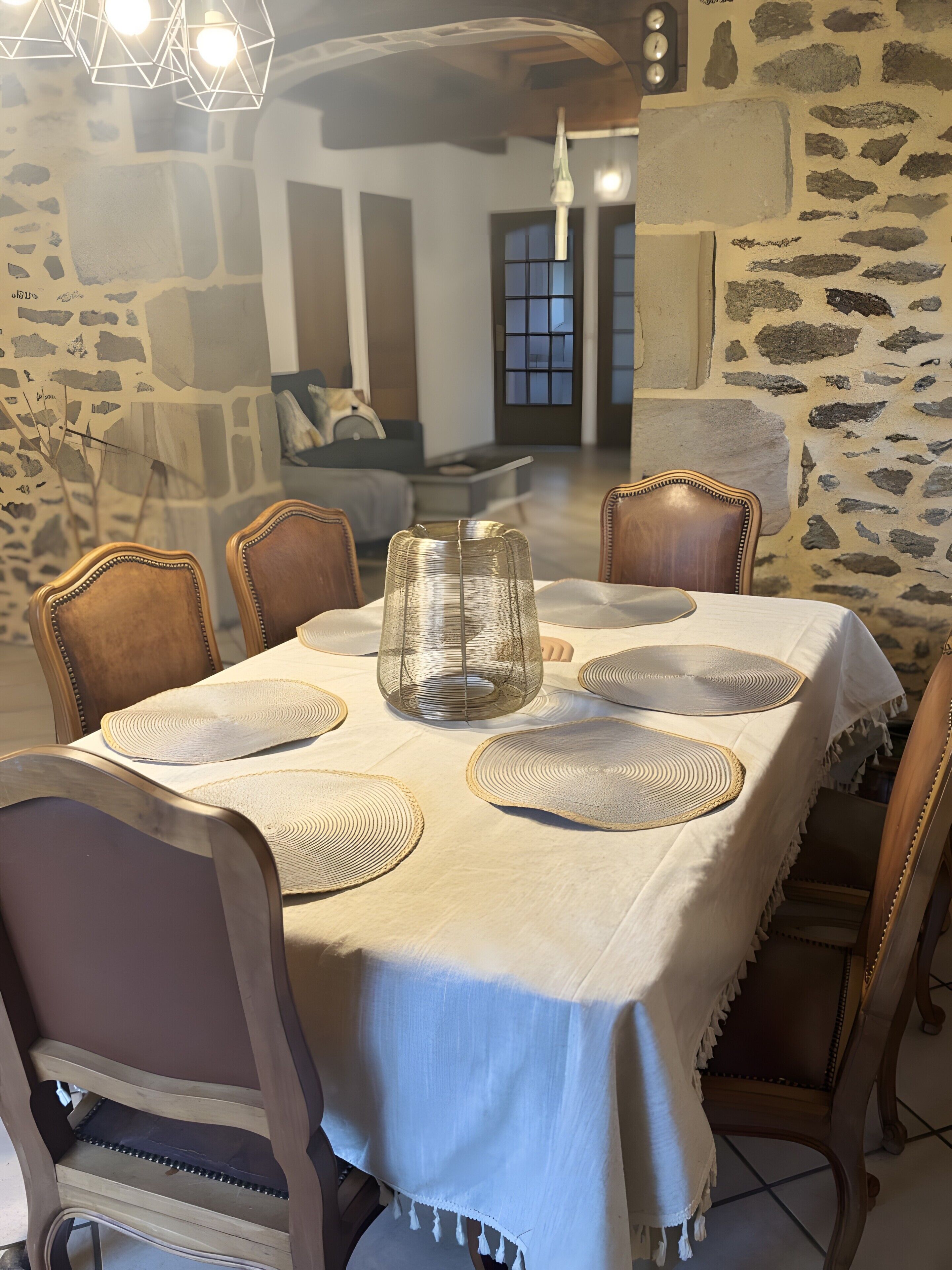 Un comedor con una mesa dispuesta para cuatro personas, sillas alrededor, un centro de mesa de cristal decorativo y una pared de piedra.