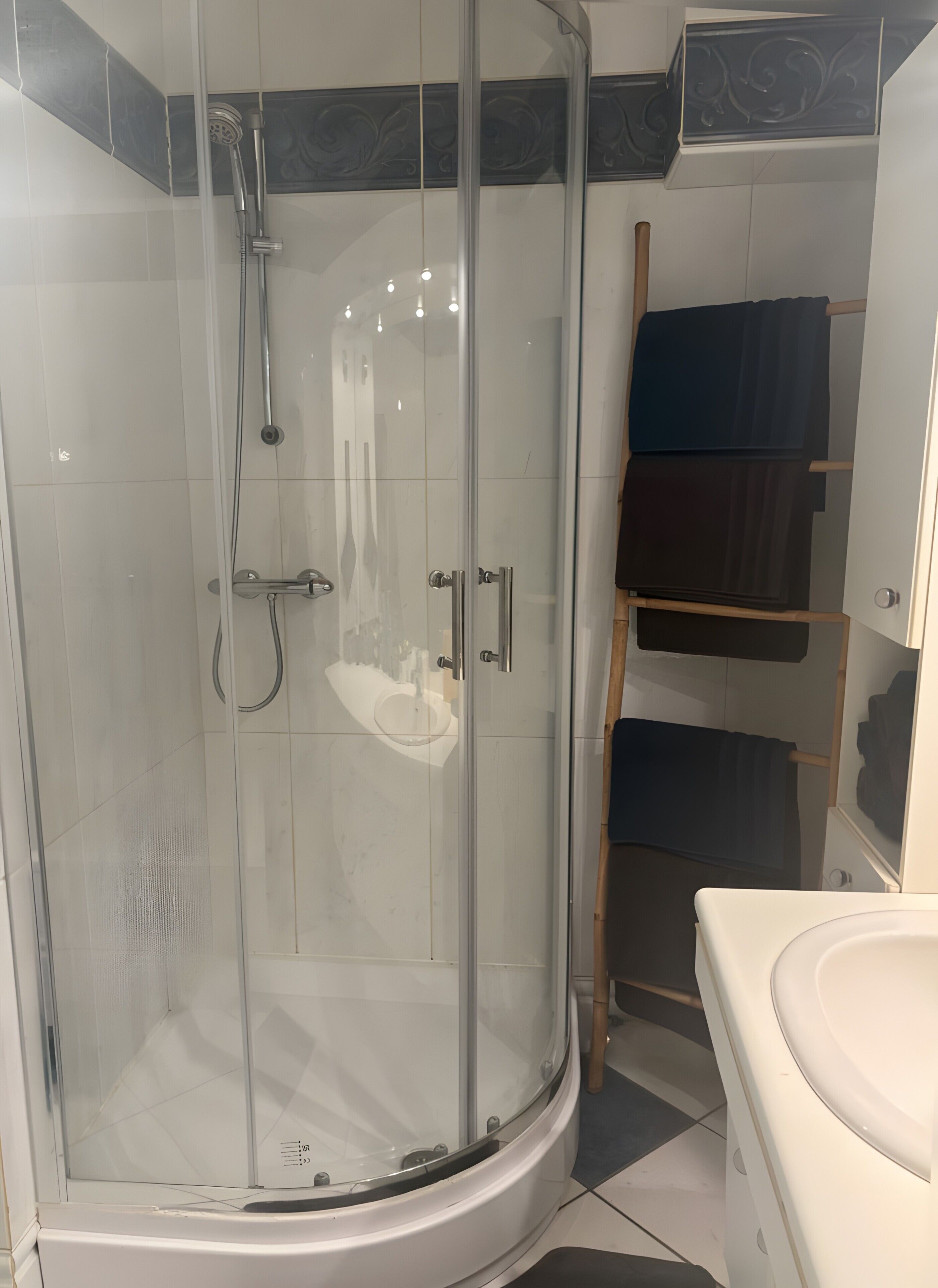 A glass-enclosed shower with a handheld showerhead, a white sink, and a towel rack.