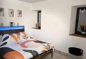Ein Schlafzimmer mit einem Bett, einem Regal mit Dekorationen, einem Spiegel und einem Mülleimer.