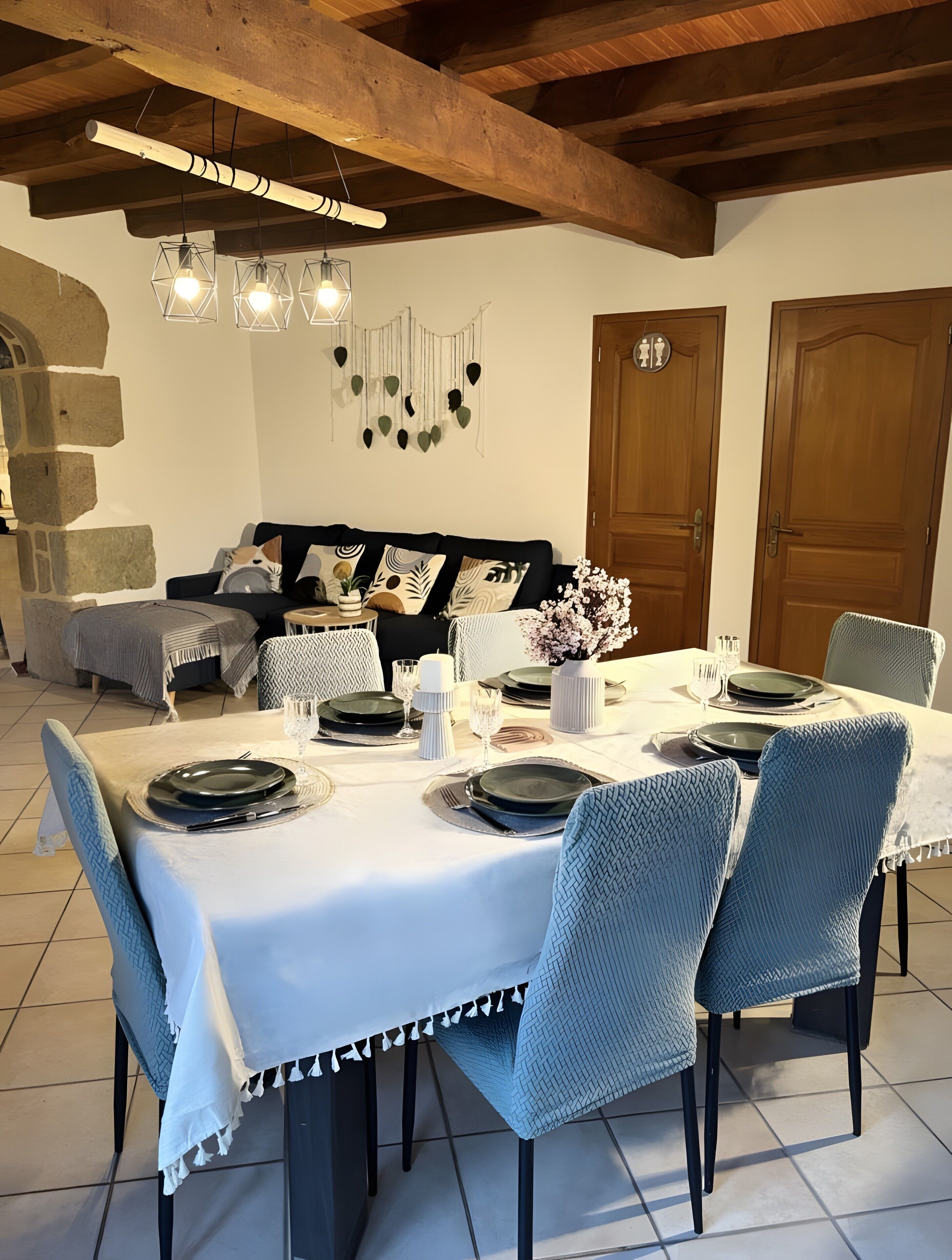 A dining area with a table set for four, chairs, a wooden ceiling, and a stone wall.