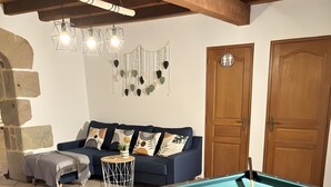 Ein Billardtisch mit Kugeln, eine Couch mit Kissen, ein kleiner runder Tisch und eine Wandleuchte.