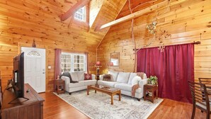 A cozy log cabin interior with a wooden ceiling, a white sofa, a coffee table, and a television on a wooden cabinet. - Wildcat Retreat, Cozy Norris Lake Cabin Getaway (New Tazewell)