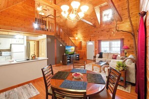 Interior de una cabaña de madera con comedor, cocina, sala de estar y una escalera.