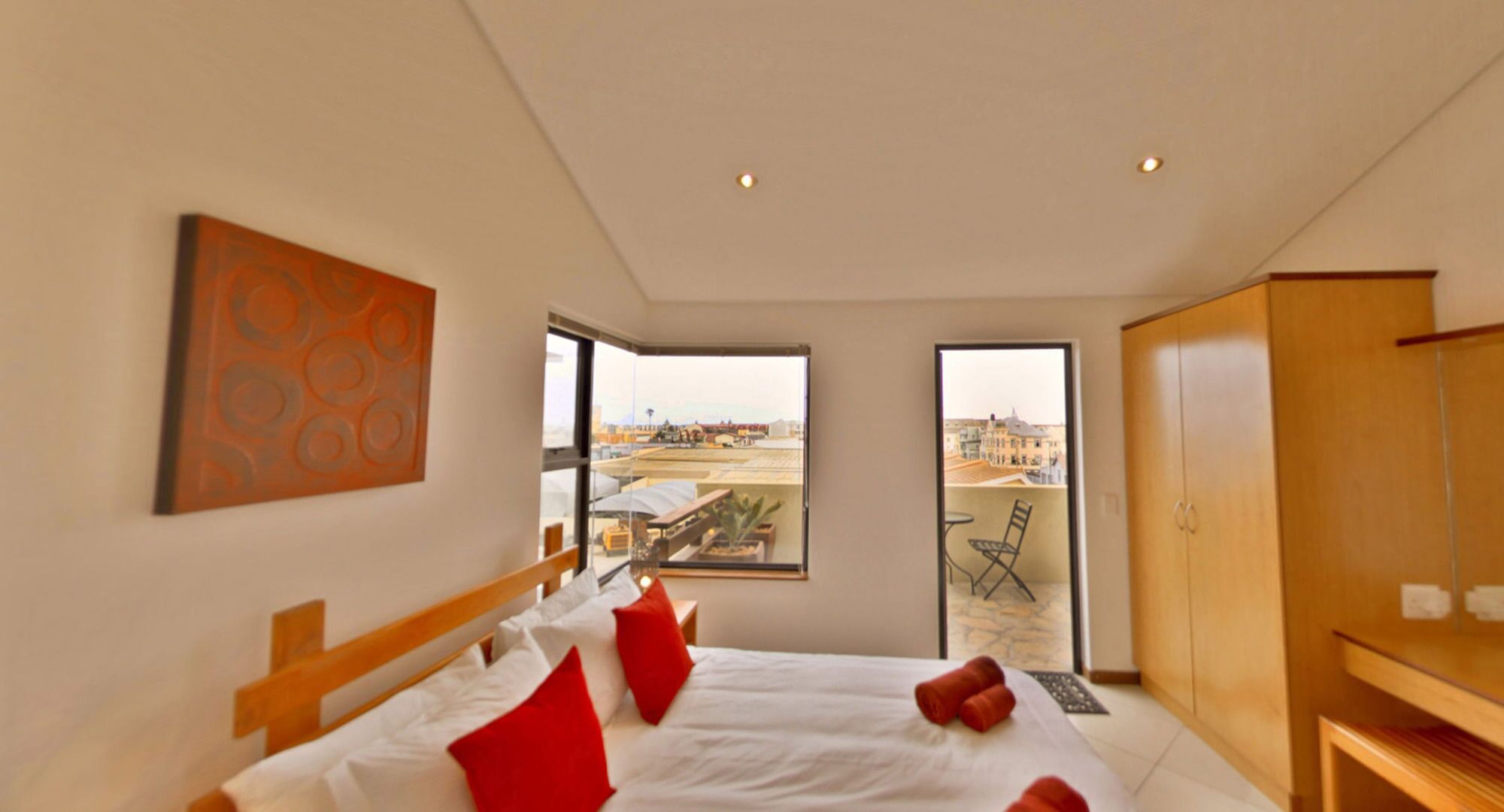 A modern bedroom with a large bed, a wooden headboard, a view of the city through a large window, and a wooden wardrobe.