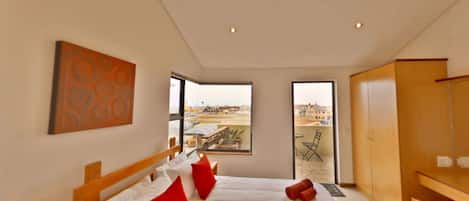 Un dormitorio moderno con una cama grande, cabecera de madera, vistas de la ciudad a través de un ventanal amplio y un armario de madera.