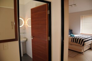 A room with a wooden door, a toilet, and a bed with a striped blanket. - Moringa Gardens (Swakopmund)