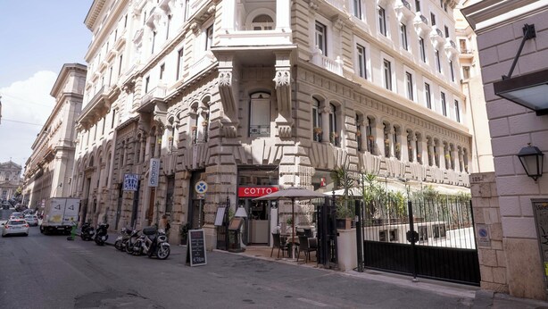 Ein historisches Gebäude mit klassischer Architektur, ein Restaurant namens 'COTTO' im Erdgeschoss und eine Straße mit geparkten Fahrzeugen.