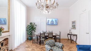 Ein Zimmer mit einem Esstisch, Stühlen, einer Chandelier, einem blauen Sofa und einer großen Küstenpflanze.