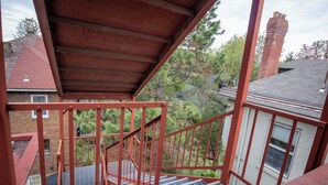 Una scala in metallo rossa che conduce a un'area riparata, con vista su una casa in mattoni e alberi.
