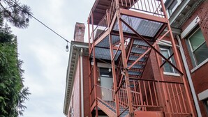Una scala antincendio rossa addossata a un edificio in mattoni con un recinto di legno davanti.