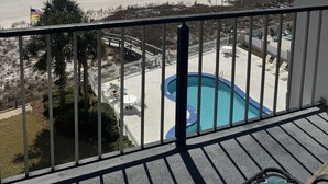 A balcony with a view of a beach, a pool, and a flag. - Breakers C52 - Direct Gulf Front (Orange Beach)