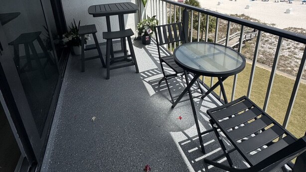 A balcony with a glass table and chairs, overlooking a beach with umbrellas and a cloudy sky. - Breakers C52 - Direct Gulf Front (Orange Beach)