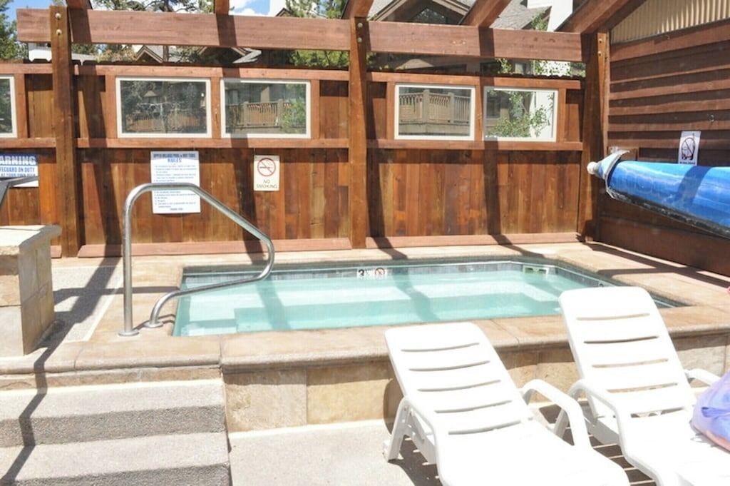 A pool area with a wooden fence, a pool with a metal ladder, and white lounge chairs.
