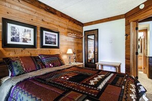 Ein gemütliches Schlafzimmer mit Holzwänden, einem großen Bett mit einer gemusterten Steudecke und zwei gerahmten Bildern an der Wand.
