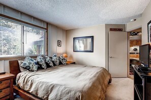 A bedroom with a bed, a nightstand, a TV, and a door leading to a kitchen. - Powder Ridge 208 - close to lifts and town! (Breckenridge)