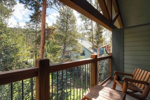 Eine Holzterrasse mit Geländer, einer Bank und Blick auf eine bewaldete Gegend mit Häusern im Hintergrund.