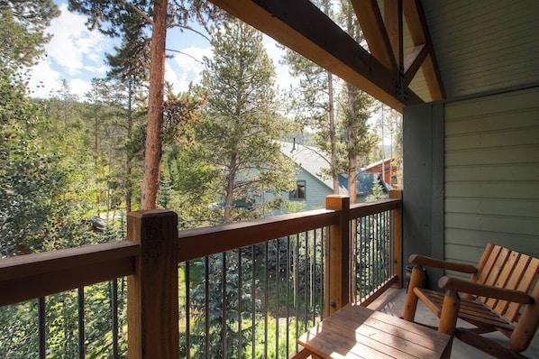 A wooden deck with a railing, a bench, and a view of a forested area with houses in the background. - Powder Ridge 208 - close to lifts and town! (Breckenridge)