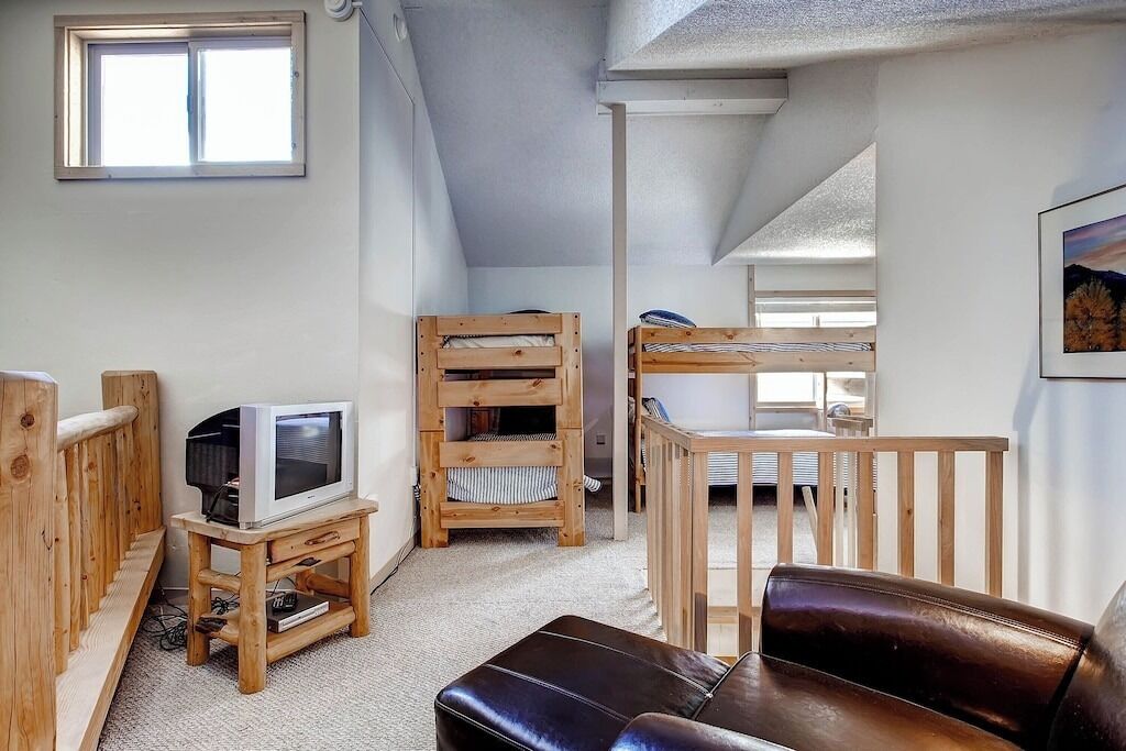 Ein gemütliches Zimmer mit einem Holz-Fernsehmöbel, einer Ledersofa und einem Etagenbett.