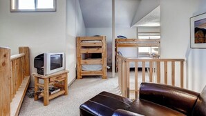 Ein gemütliches Zimmer mit einem Holz-Fernsehmöbel, einer Ledersofa und einem Etagenbett.