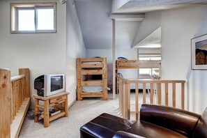A cozy room with a wooden TV stand, a leather couch, and a bunk bed. - Powder Ridge 208 - close to lifts and town! (Breckenridge)