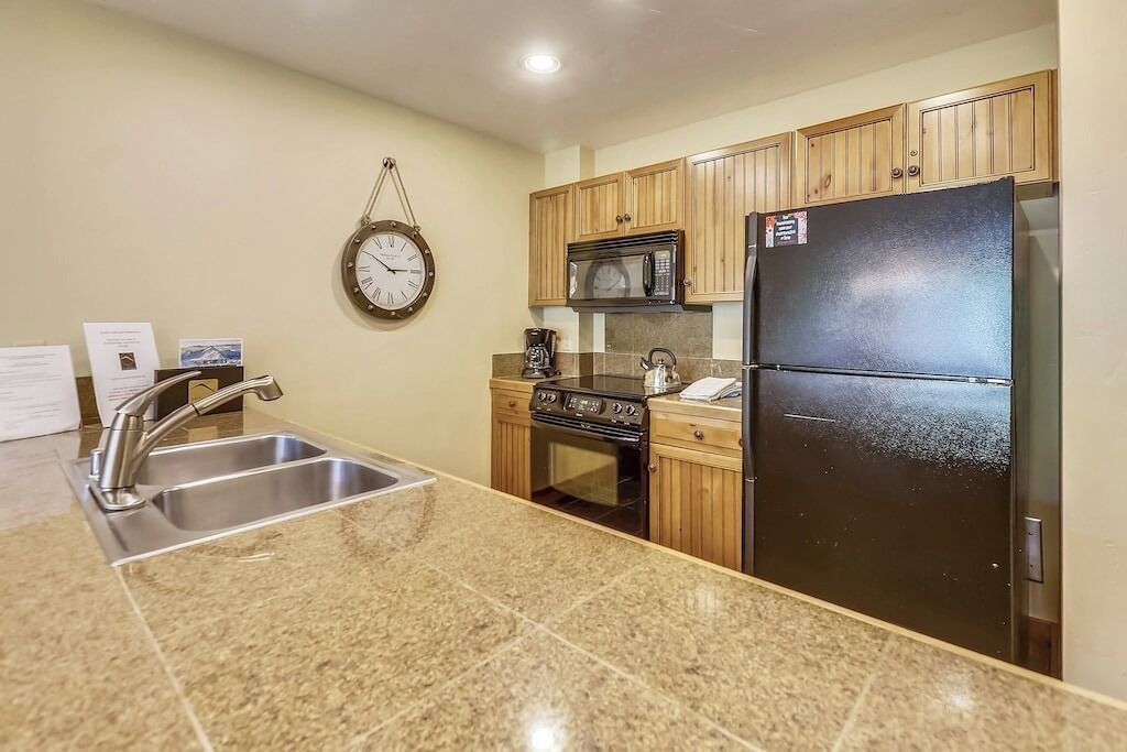 A kitchen with granite countertops, stainless steel appliances, wooden cabinets, and a wall-mounted clock.