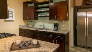 A kitchen with dark wooden cabinets, a stainless steel refrigerator, a granite countertop, and a coffee maker. - Little Cay – A Sweet Family Escape Ocean View (Cruz Bay)