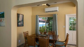 A dining area with a table and chairs, an air conditioning unit, and a view of the outdoors. - Little Cay – A Sweet Family Escape Ocean View (Cruz Bay)