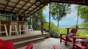 A wooden deck with red Adirondack chairs and a bar area with stools. - Little Cay – A Sweet Family Escape Ocean View (Cruz Bay)