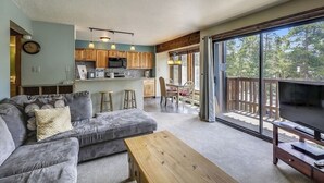 A modern living room with a grey sofa, wooden coffee table, and a balcony with a TV. - Four O'Clock Lodge Condo- close to lifts and town! (Breckenridge)