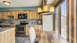 A kitchen with wooden cabinets, a built-in microwave, a stove, and a dining area with a wooden table and chairs. - Four O'Clock Lodge Condo- close to lifts and town! (Breckenridge)