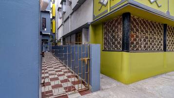 A narrow alleyway with a checkered tile floor leading to a building with a yellow facade and a decorative window grille.