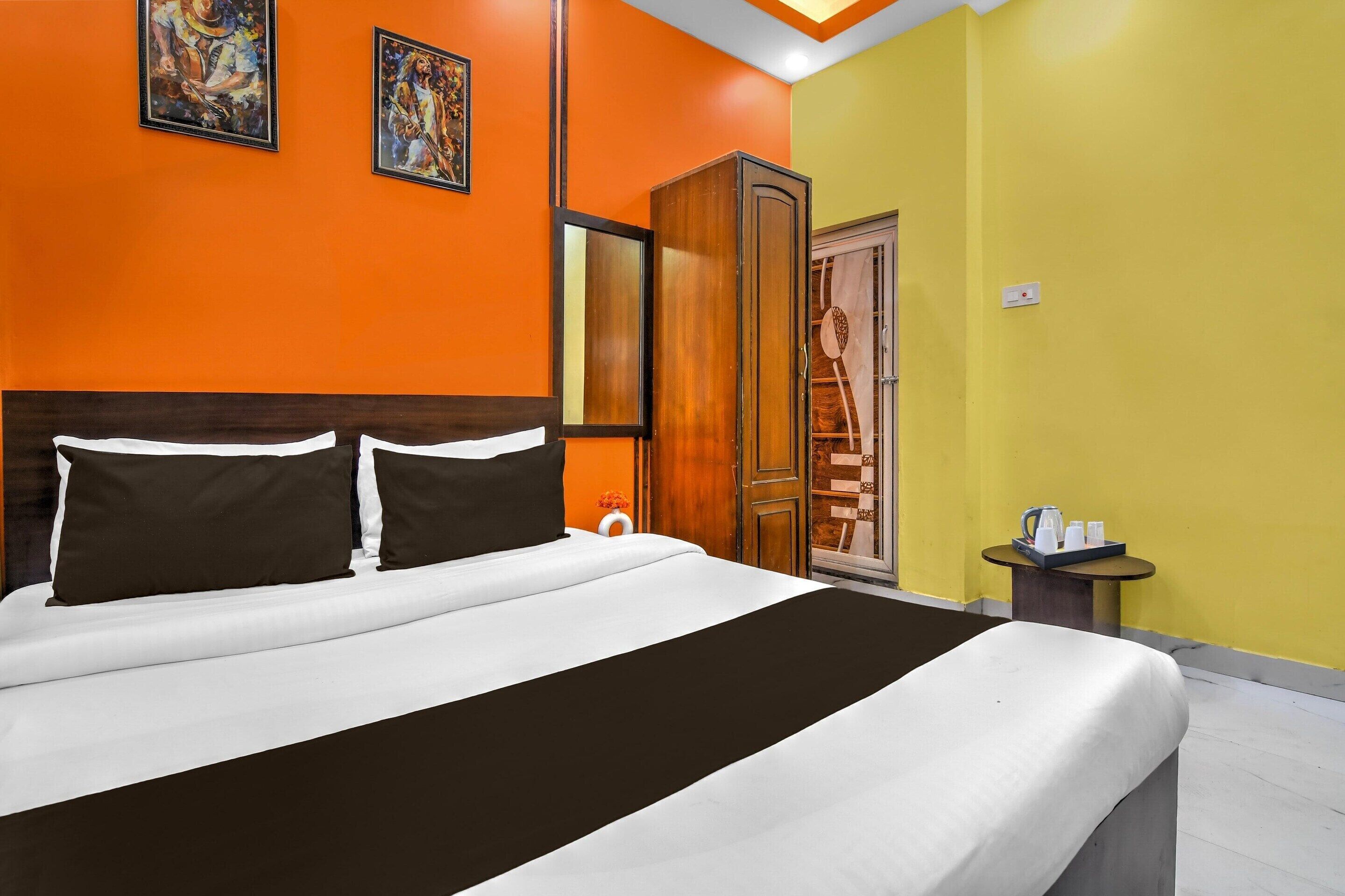 Una habitación de hotel con cama, un armario, una mesita con una tetera y una pared decorada con dos cuadros.