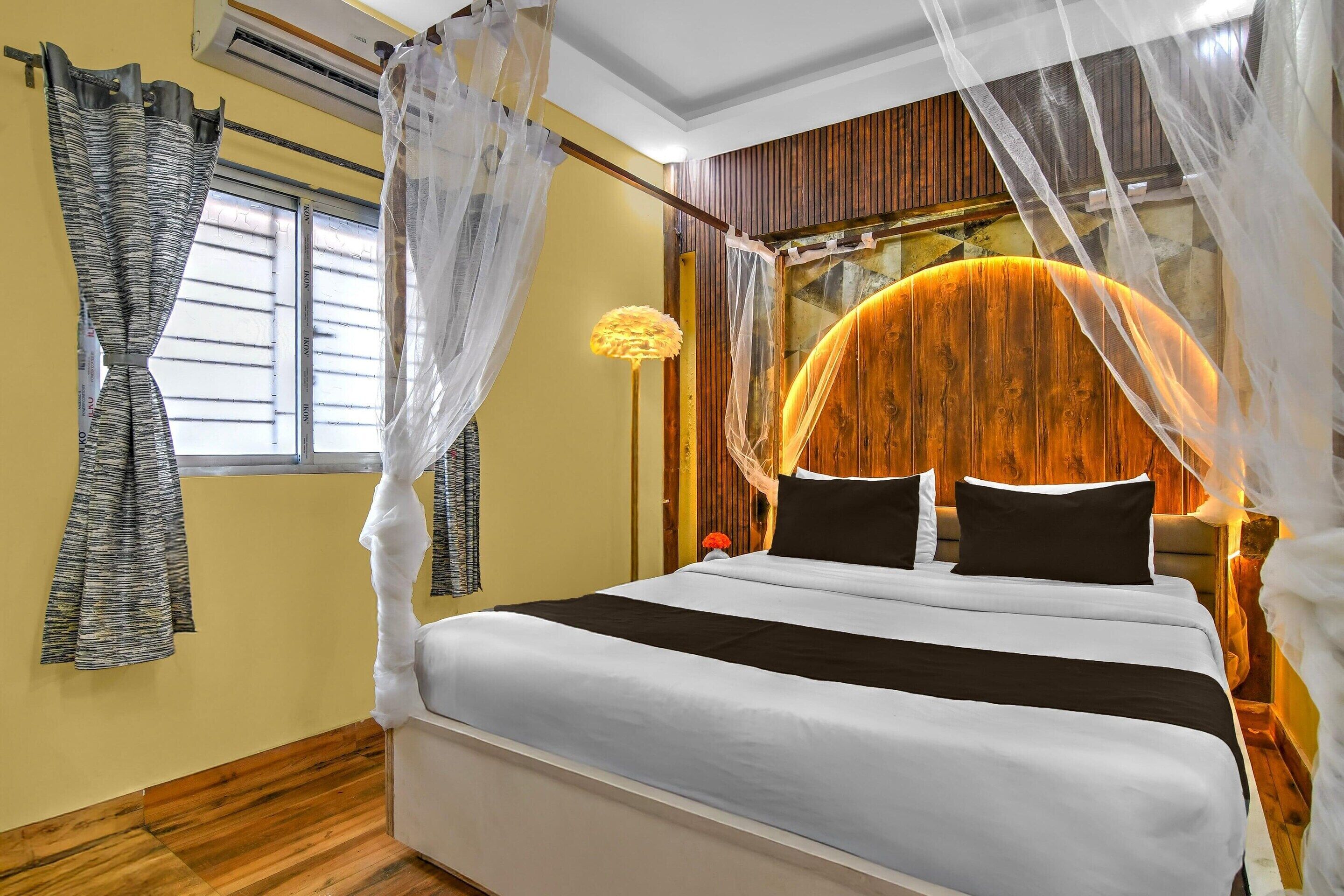 A bedroom with a bed, curtains, a nightstand, and a wall-mounted lamp.