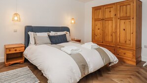 A bedroom with a large bed, wooden wardrobe, two bedside tables, and two wall-mounted lamps. - Shamrock (Exeter)