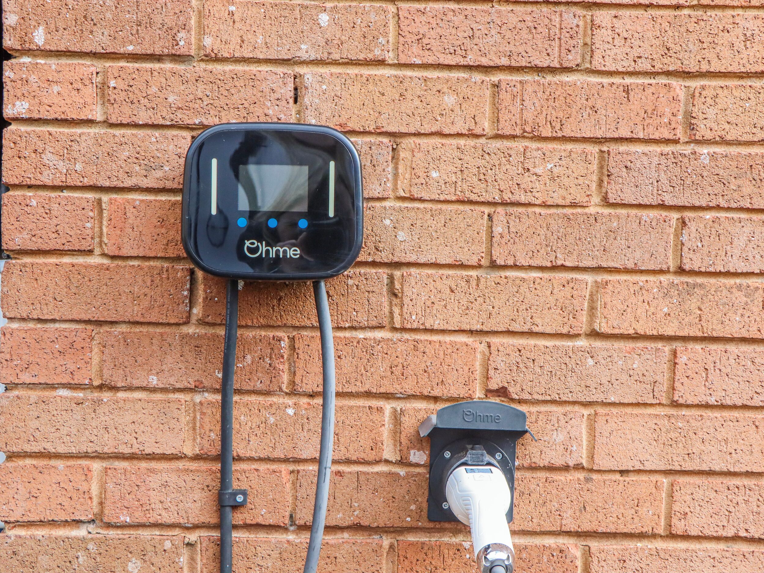 Eine Ziegelwand mit einer Ladestation für Elektrofahrzeuge, gekennzeichnet mit "Ohme" und einem digitalen Bildschirm.