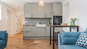 A modern kitchen with grey cabinets, a Bosch oven, and a patterned backsplash. There is a dining area with a table and chairs, and a blue sofa with patterned cushions. - Shamrock (Exeter)