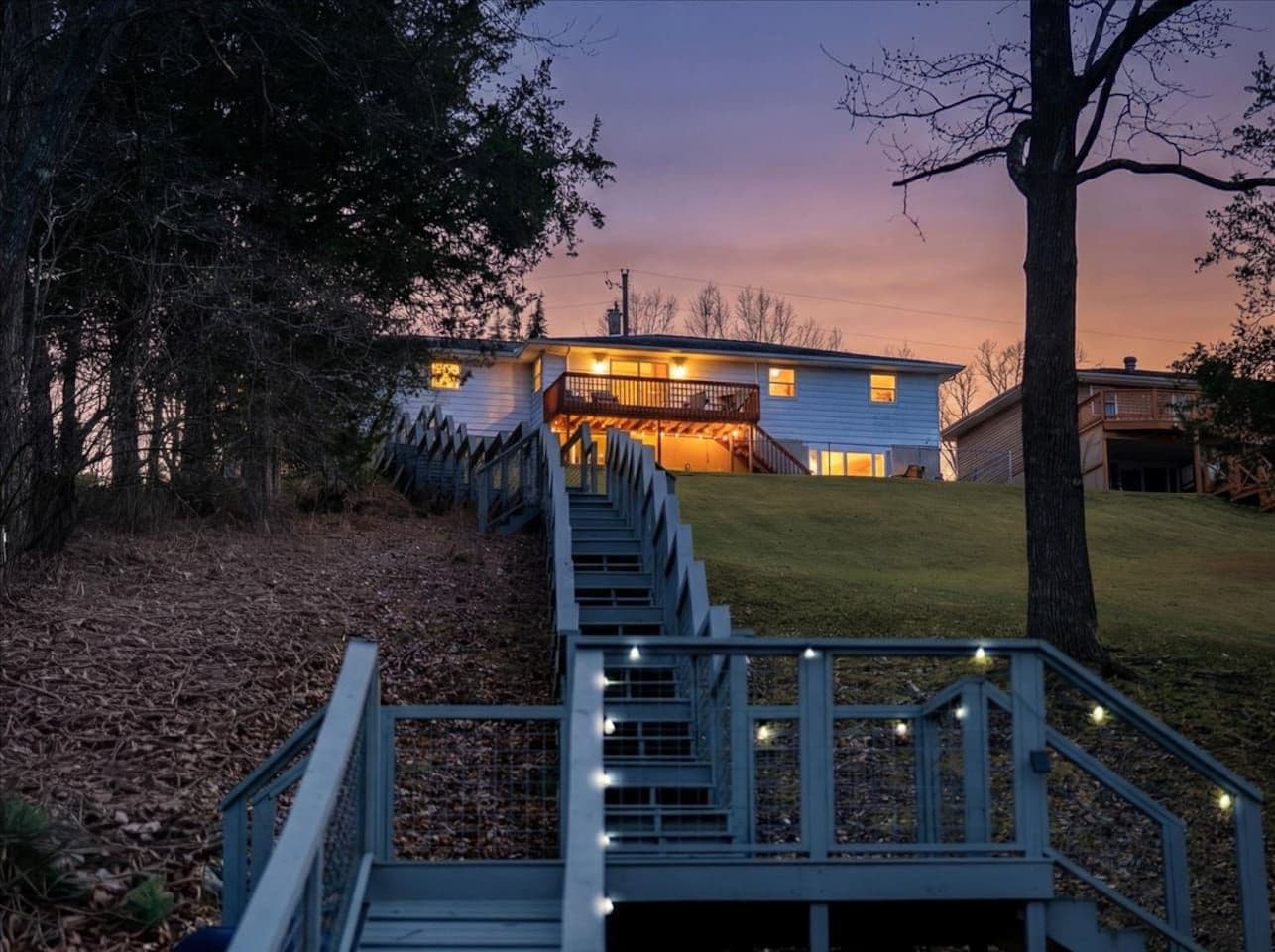 A house with a staircase leading to a front door, surrounded by trees and a grassy area.