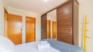 A bedroom with a bed, two wooden doors, a large mirror, and a yellow coat rack. - Apartments in Jd. Centenario in Pocos de Caldas - Clds (Poços de Caldas)