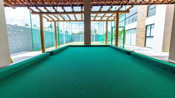 An indoor pool area with a green pool surface, wooden pergola overhead, and a view of a building with large windows and a brick wall in the background.