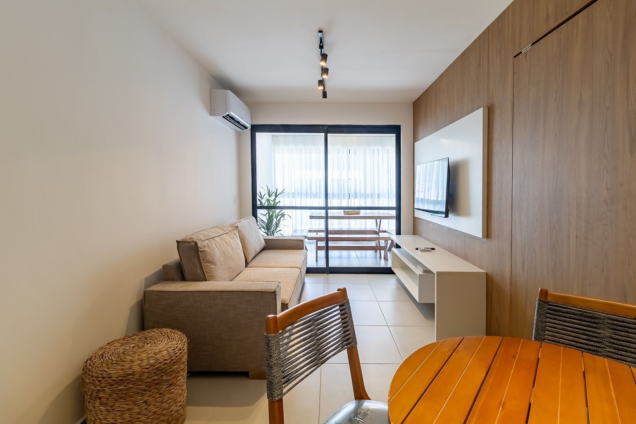 A modern living room with a sofa, a dining table, a TV, and a large window.