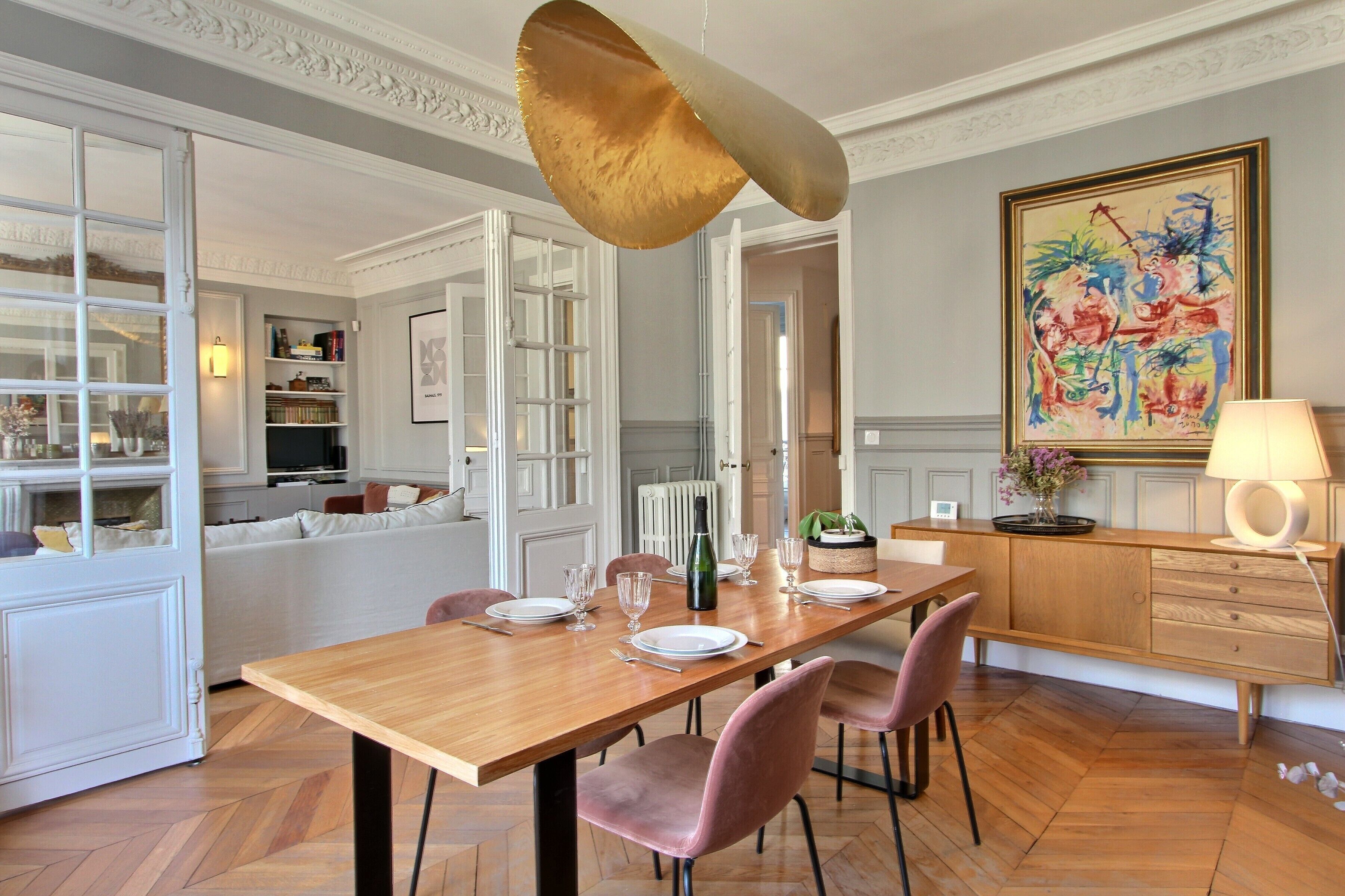 Ein Essbereich mit einem Holztisch, gedeckt für vier Personen, umgeben von rosa Stühlen, einer Chandelier und einem Gemälde an der Wand.