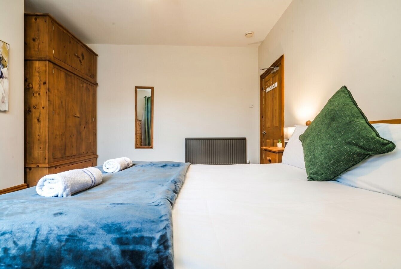 A bedroom with a bed, a wooden wardrobe, a radiator, and a green pillow.