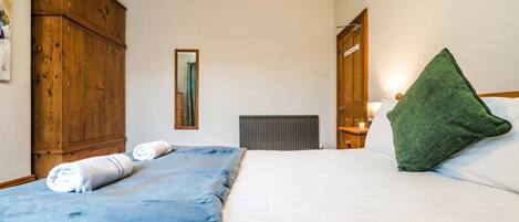 A bedroom with a bed, a wooden wardrobe, a radiator, and a green pillow.