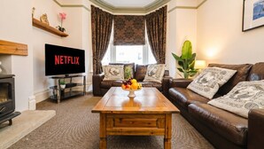 Ein Wohnzimmer mit Couch aus braunem Leder, einem Holztisch, einem Fernseher und einem Kamin.
