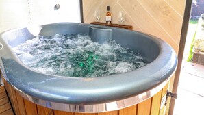 A hot tub with a wooden interior, a bottle of wine, and a glass on a wooden shelf. - Old Rosie (Grantham)