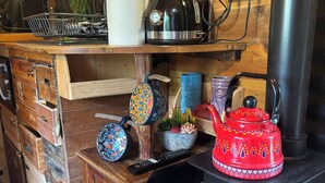 A rustic kitchen with a wood-burning stove, a kettle, colorful teapots, and a remote control. - Old Rosie (Grantham)
