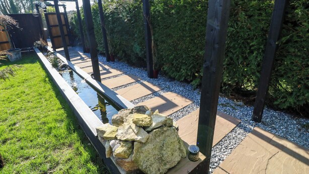 A garden with a stone pathway, a small pond, and a wooden pergola structure. - Old Rosie (Grantham)