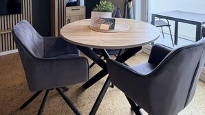 Un comedor moderno con una mesa redonda, cuatro sillas, una lámpara colgante y vistas a una masa de agua a través de ventanas amplias.