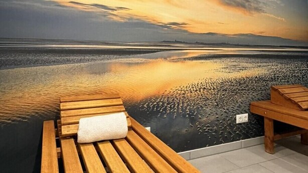 Una habitación con un gran mural de un atardecer sobre el agua, bancos de madera y piso de baldosas.